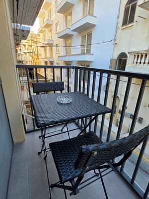 Ein Balkon mit Tisch und zwei Stühlen, einem Geländer und Blick auf benachbarte Gebäude.