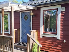 Ein rotes Holzgebäude mit einer blauen Tür, einem Fenster und einer Holztreppe, die zu einer Veranda führt.