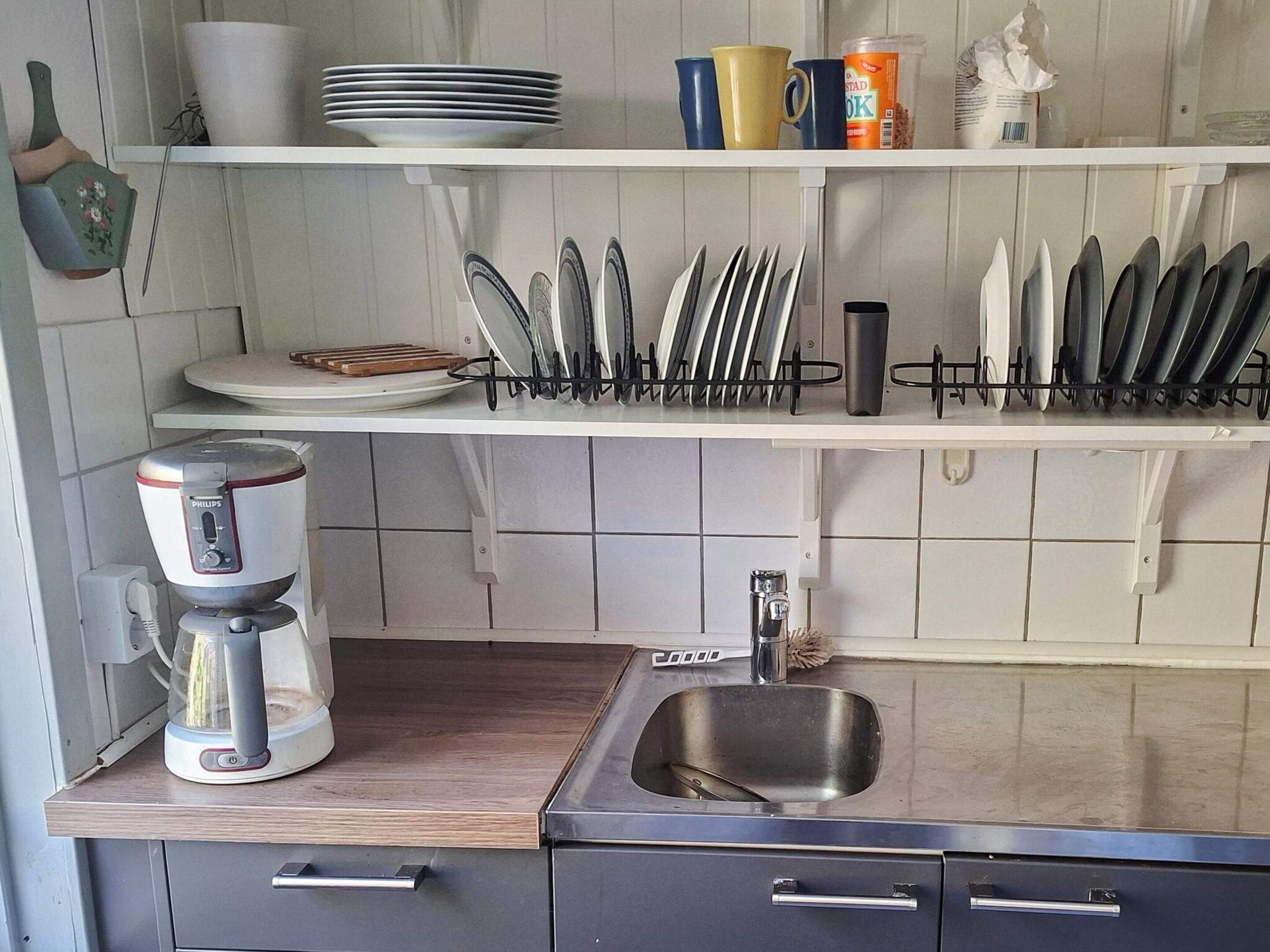 A kitchen with a coffee maker, a sink, and utensils on shelves.