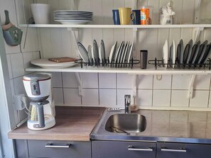 Uma cozinha com cafeteira, pia e utensílios em prateleiras.