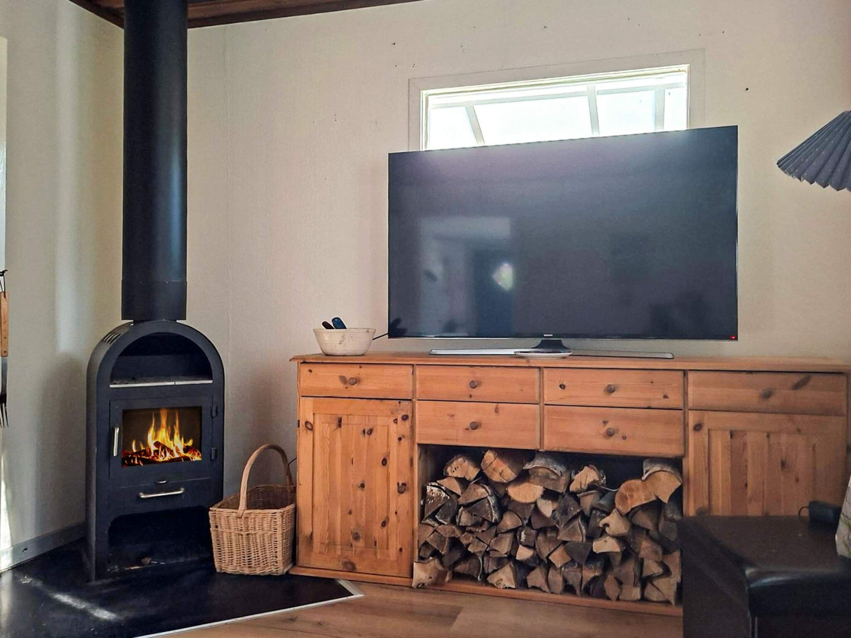 Una sala de estar con una estufa de leña, un televisor y una pila de leña.