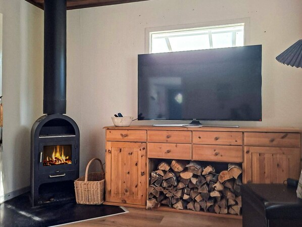 Una sala de estar con una estufa de leña, un televisor y una pila de leña.