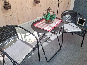 Um pequeno pátio externo com uma mesa redonda, duas cadeiras e uma planta decorativa.