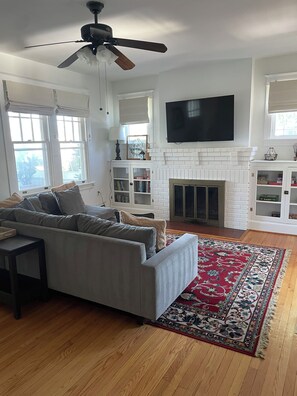 A living room with a sofa, a fireplace, a television, and a ceiling fan. - Spa Creek Cottage – Walk to Downtown Annapolis (Annapolis)