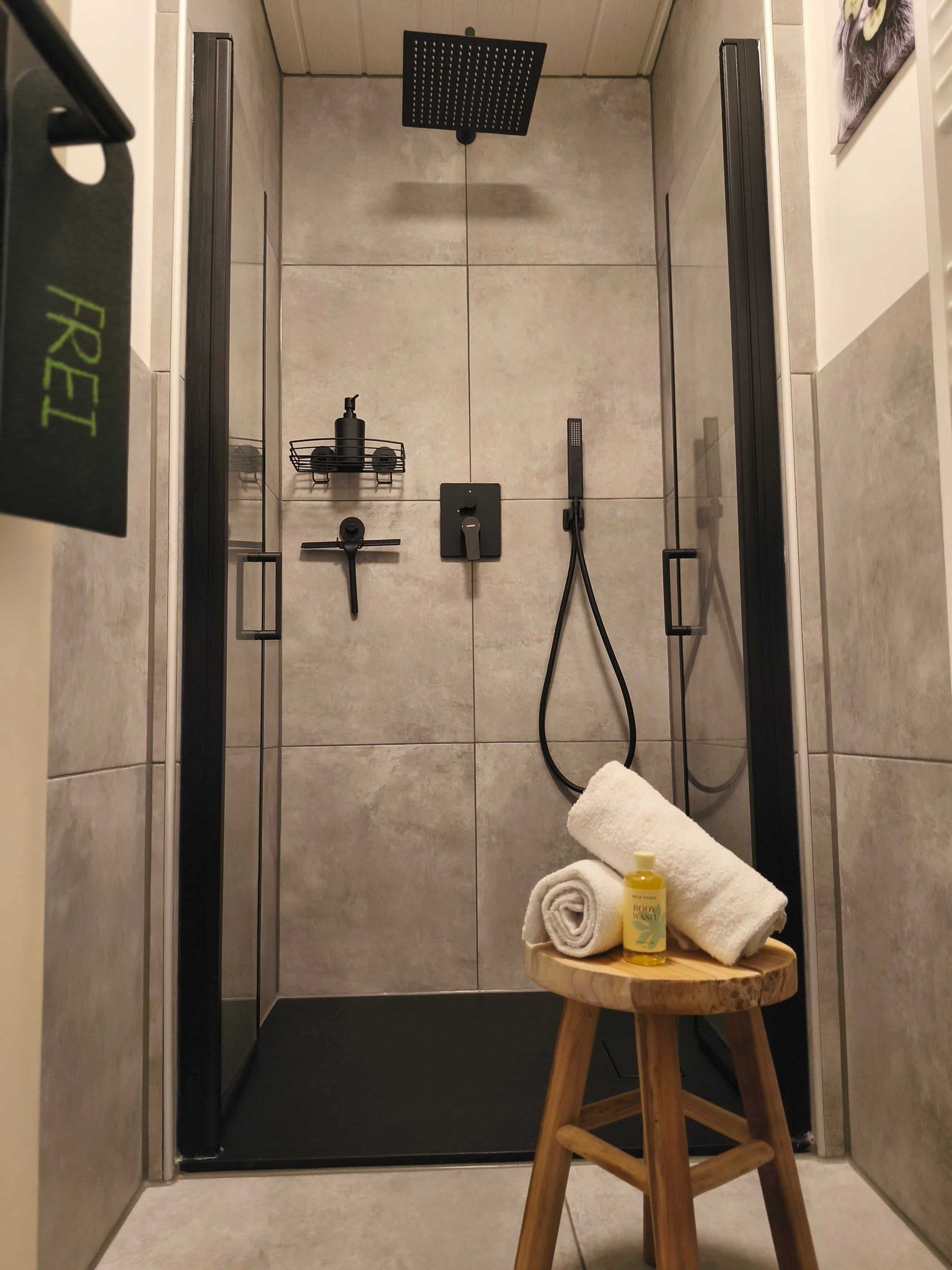 Un espace douche équipé d’un pommeau de douche noir, d’un pommeau de douche à main et d’une serviette posée sur un tabouret.