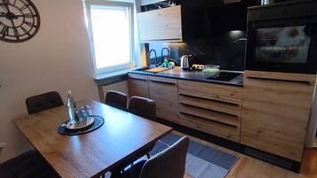 Una cocina moderna con zona de comedor, armarios de madera, un reloj grande y una ventana.