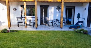Katettu terassi, jossa on ulkokalusteita, ovi ja pieni puutarha-alue.