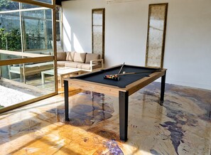 A pool table with a wooden frame and black legs, a sofa, and a glass door leading to an outdoor area. - Diamant - Exclusive Villa (Funchal)