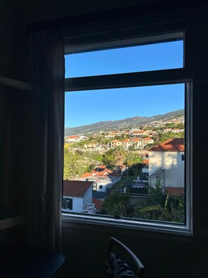 A room with a large window offering a view of a hillside town with buildings and greenery. - Diamant - Exclusive Villa (Funchal)