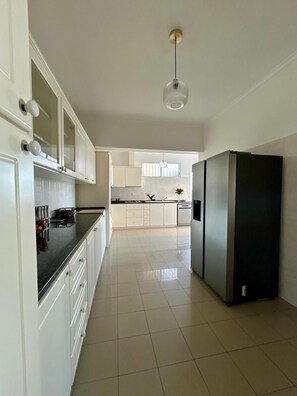 A kitchen with white cabinets, a black refrigerator, and a hanging light fixture. - Diamant - Exclusive Villa (Funchal)