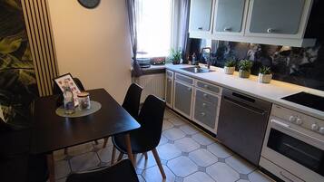 A modern kitchen with a dining area, featuring hexagonal tiles, a built-in oven, and a window with curtains.