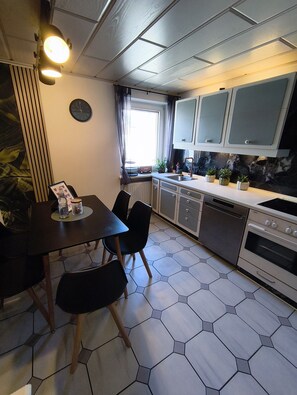 A modern kitchen with a dining area, featuring hexagonal tiles, a built-in oven, and a window with curtains. - House 113 - Burgperle Vacation Rental, Burghausen, 24-Hour Self-Check-In (Burghausen)