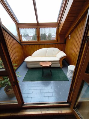 Una habitación con interior de madera, un sofá blanco, una mesita redonda y vistas a través de un ventanal.