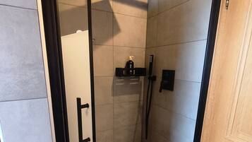 Un espace douche moderne doté d’une porte en verre, d’un pommeau de douche à main et d’un sèche-cheveux portatif.