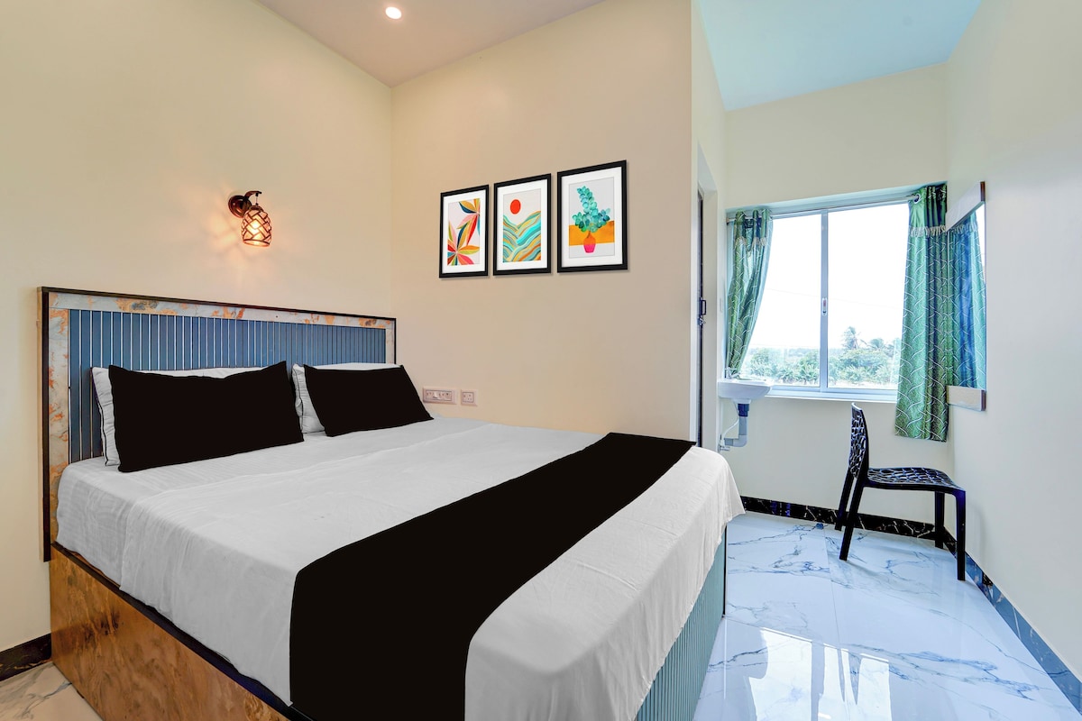 A bedroom with a bed, a wall-mounted light fixture, a window with curtains, and a small chair.