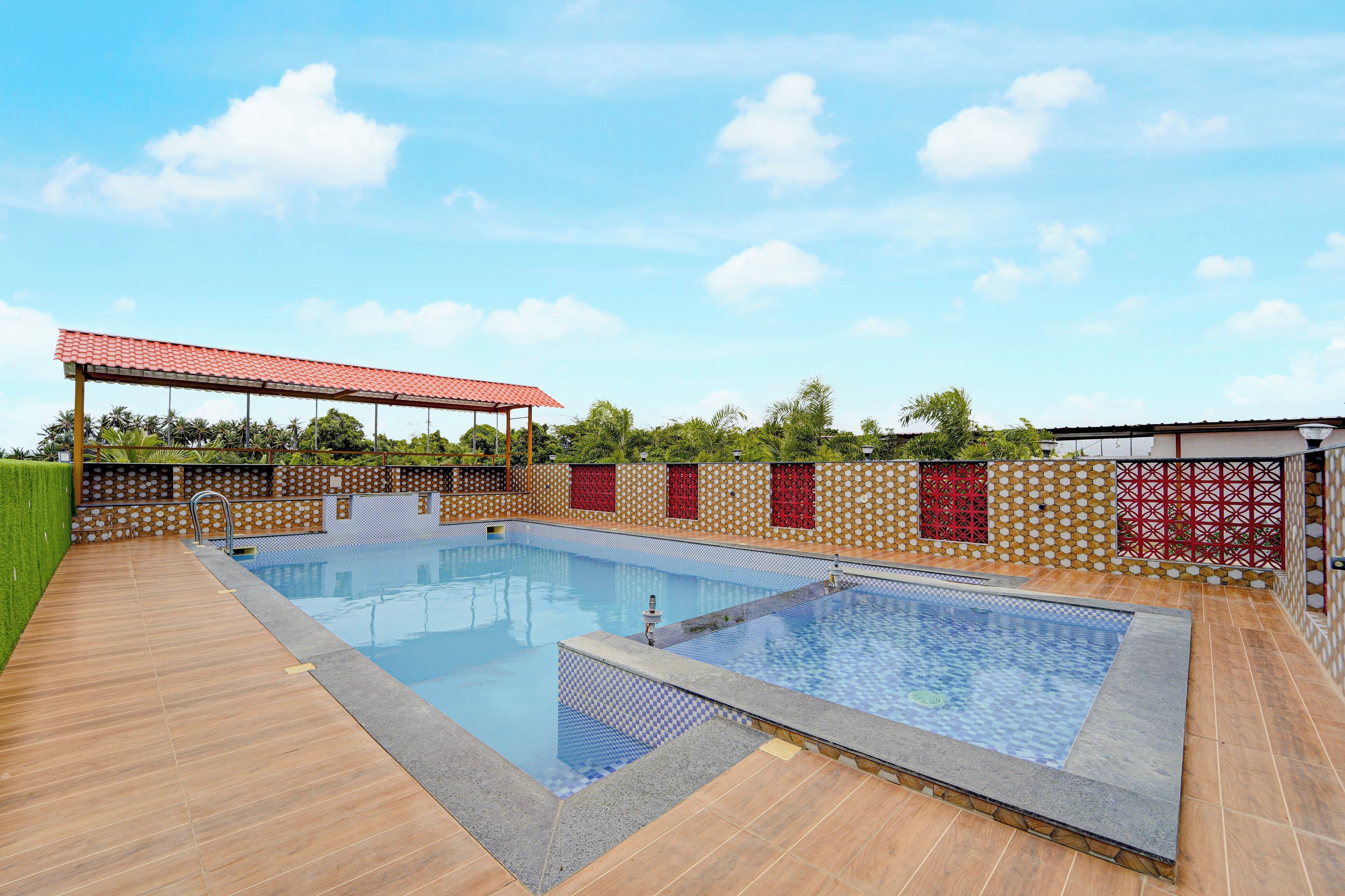 Una piscina rectangular con un borde de baldosas, un área de estar cubierta y una pared decorativa con patrones geométricos.
