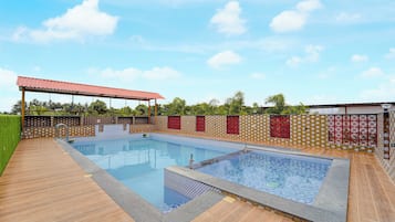 Una piscina rectangular con un borde de baldosas, un área de estar cubierta y una pared decorativa con patrones geométricos.