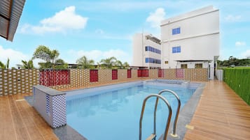 Una piscina con cubierta de madera, rodeada por un muro bajo con baldosas decorativas.