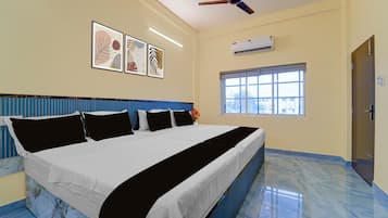 Una habitación de hotel con una cama grande, un ventilador de techo, un equipo de aire acondicionado y una ventana con persianas.