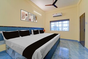 A hotel room with a large bed, a ceiling fan, an air conditioning unit, and a window with blinds. - Townhouse Kanyakumari Bus Terminal (Nagercoil)