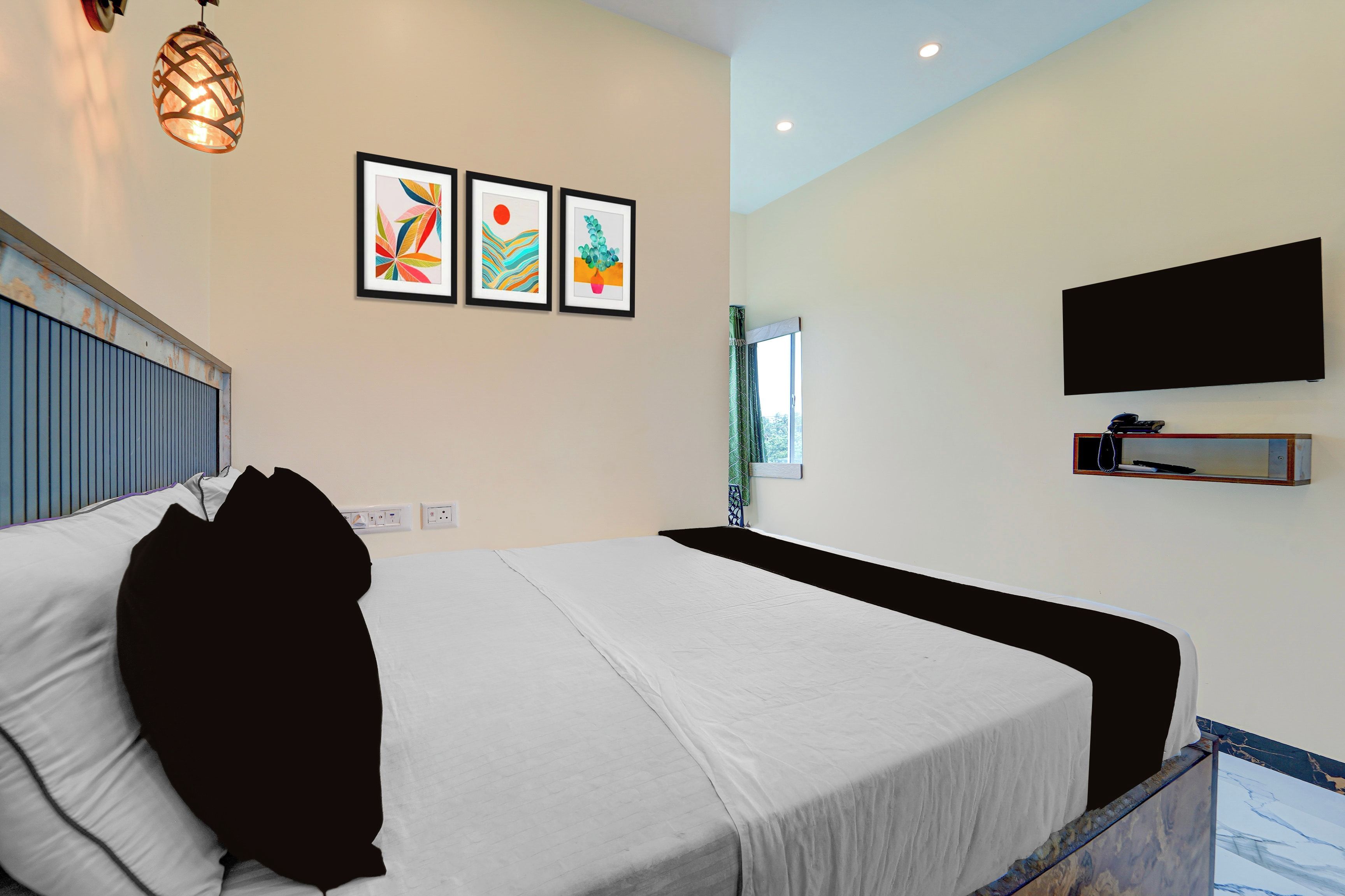 Una habitación de hotel con una cama, un televisor montado en la pared y tres cuadros enmarcados.