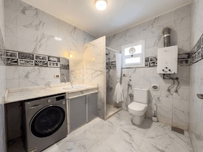 Une salle de bain équipée d’un lave-linge, de toilettes et d’une douche.