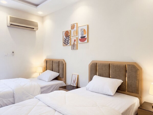Une chambre d’hôtel avec deux lits, une table de chevet, une lampe, un appareil de climatisation et des œuvres d’art accrochées au mur.
