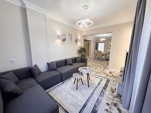 Un salon moderne avec un canapé d’angle, un tapis à motifs et un coin repas à l’arrière-plan.