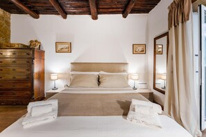 Een net opgemaakt bed met kaptondeel, twee nachtkastjes met lampen, een houten dressoir en een grote spiegel aan de muur.