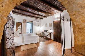 Un dormitorio con techo de madera, una cama con ropa blanca, un aparador, un escritorio con una lámpara y un armario.