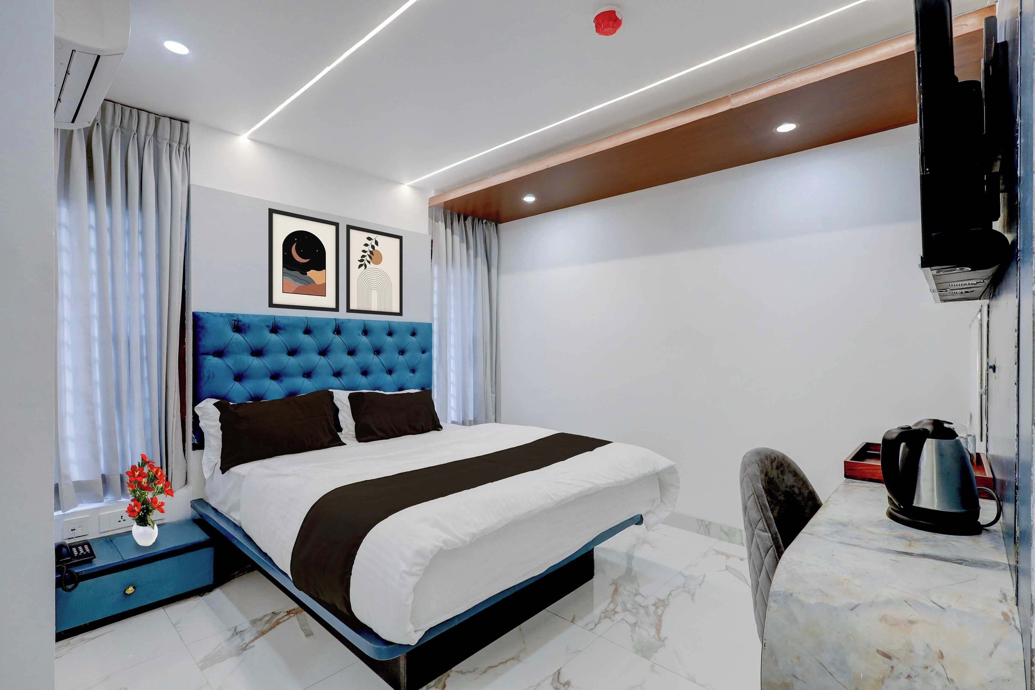 Une chambre d’hôtel moderne dotée d’un grand lit, d’un téléviseur à écran plat fixé au mur, d’un bureau avec une bouilloire et d’une petite table agrémentée d’un vase de fleurs.