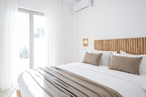 A hotel room with a large bed, a wooden headboard, and a view of the outdoors through a sliding door. - Paros villa with private pool, steps from the sea & traditional village in Aliki (Aliki - Paros)