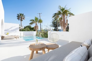 A modern outdoor pool area with lounge chairs, a fan, and a view of palm trees and a clear sky. - Paros villa with private pool, steps from the sea & traditional village in Aliki (Aliki - Paros)