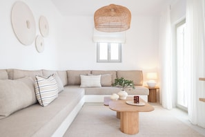 Ett modernt vardagsrum med en soffa, ett soffbord, en hängande lampa och ett fönster med persienner.