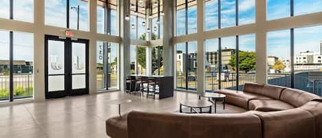 A spacious lobby with large windows, a seating area with a sofa and tables, and a visible exit door.