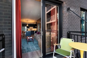 Eine moderne Wohnung mit einer Schiebetür zu einem Balkon, einer Küche mit dunklen Schränken und einem Essbereich mit einem gemusterten Teppich.