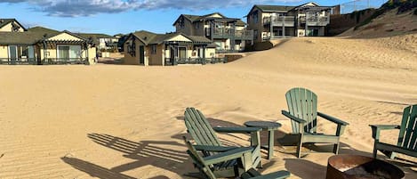 A beachside resort with multiple buildings, outdoor seating, and a fire pit.