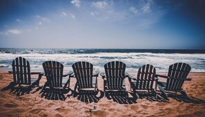 Four Adirondack chairs lined up on a sandy beach with the ocean in the background. - 500 feet from Beach: 2BR with Resort Amenities (Marina)