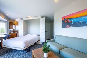 A hotel room with a bed, a sofa, a desk, a chair, and a painting of a sunset over the ocean. - 500 feet from Beach: 2BR with Resort Amenities (Marina)