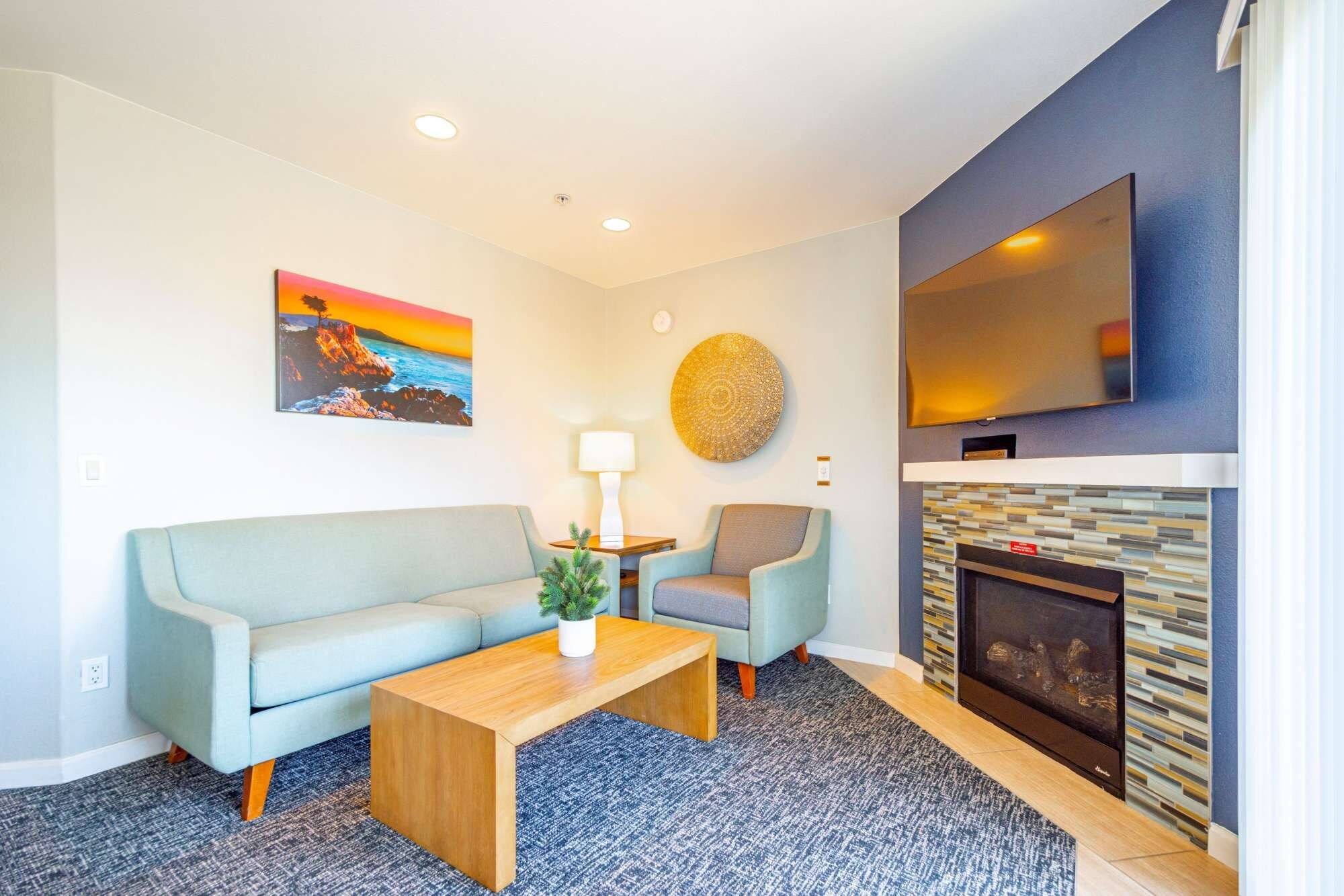 A living room with a sofa, armchair, coffee table, fireplace, TV, and artwork.