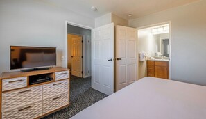 A hotel room with a bed, a TV on a wooden cabinet, a bathroom with a mirror, and a door leading to another room. - 500 Feet from Beach. 2BR with Resort Amenities. (Marina)