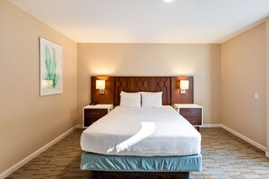 Een hotelkamer met een groot bed, twee nachtkastjes, een hoofdbord met ingebouwde verlichting en een kunstwerk in een lijst aan de muur.