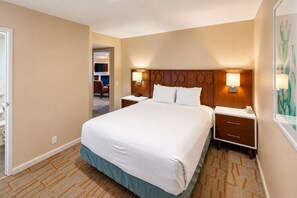 Habitación de hotel con una cama grande, mesitas de noche, una lámpara de pared y una puerta.