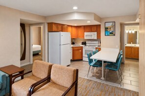 Een compacte hotelkamer met kitchenette, een eethoek met blauwe stoelen, een sofa en een bed.