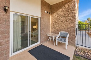 Un balcón con puerta corrediza de vidrio, una mesita redonda, dos sillas y un muro de piedra.