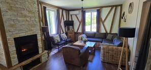 A cozy living room with a stone fireplace, wooden beams, a sofa, and a television. - Spacious vacation home (sleeps 10) near Gérardmer – ideal for groups and pets (Granges-Aumontzey)