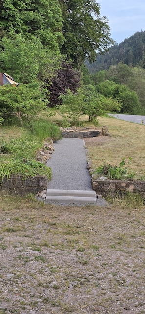 A gravel path leading to a building with a sloped roof, surrounded by greenery and a forested hillside. - Spacious vacation home (sleeps 10) near Gérardmer—ideal for groups and pets (Granges-Aumontzey)