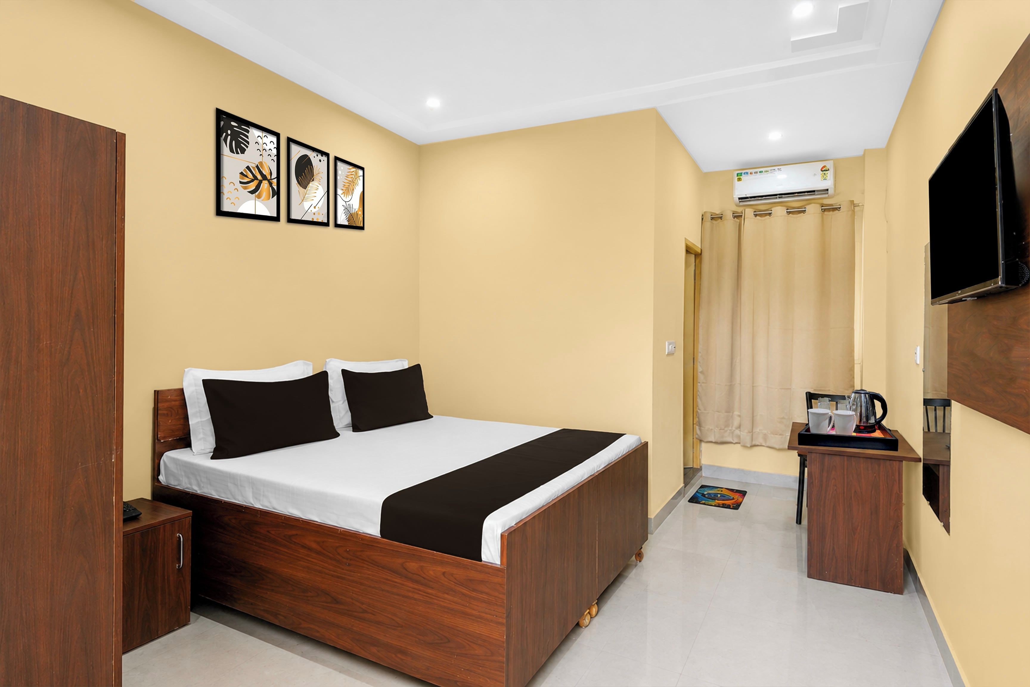 A hotel room with a wooden bed, a flat-screen TV, a coffee machine, and a bathroom with a curtain.