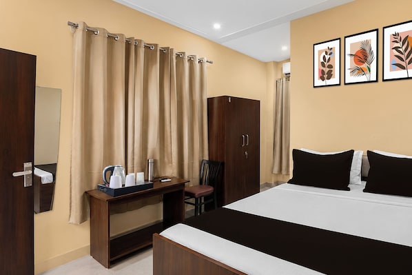 A hotel room with a bed, a desk with a kettle and cups, a wardrobe, and curtains.