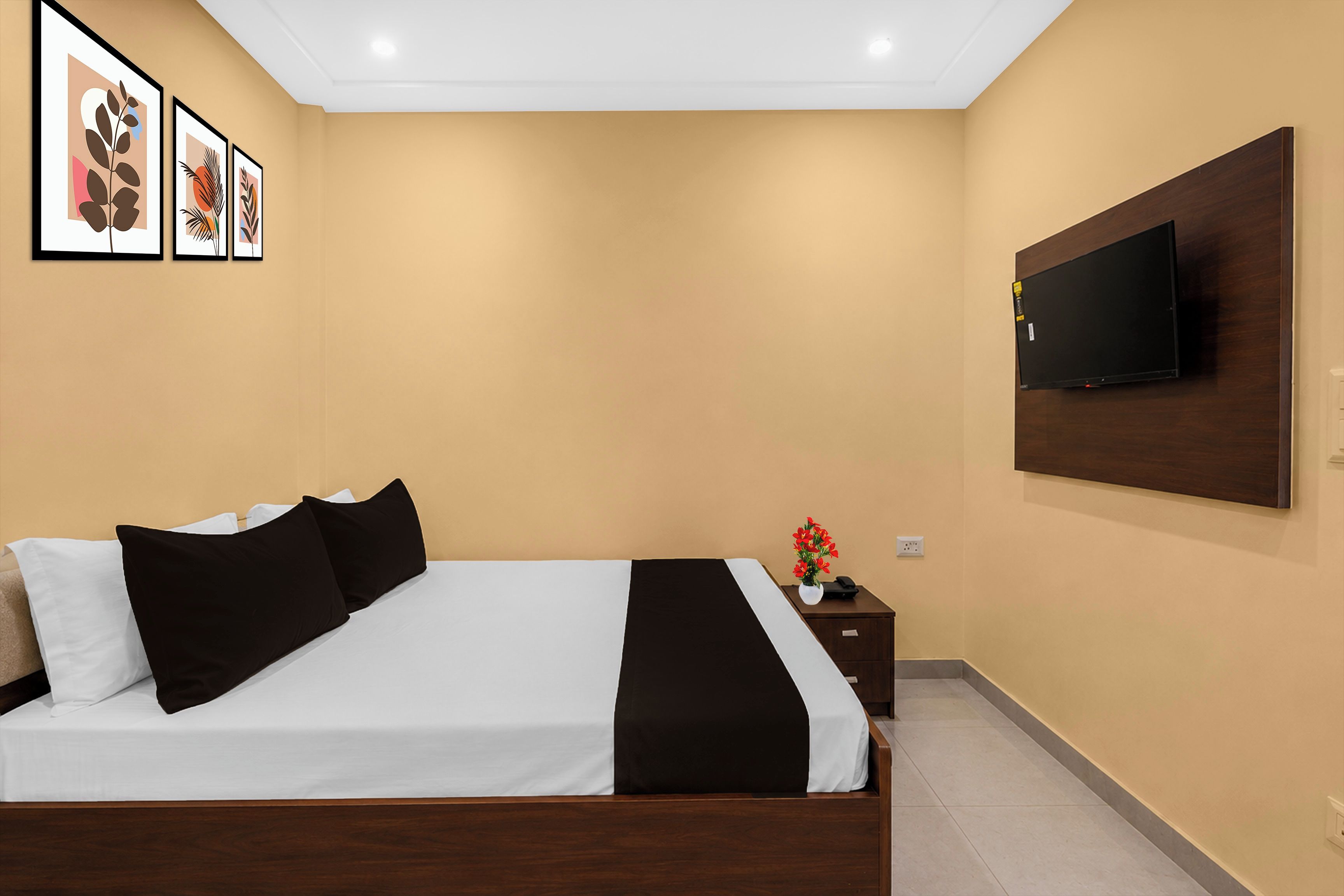 A hotel room with a bed, a nightstand, a TV mounted on the wall, and framed artwork on the wall.